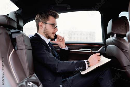 Businessman writing in notebook in luxury car © Prostock-studio