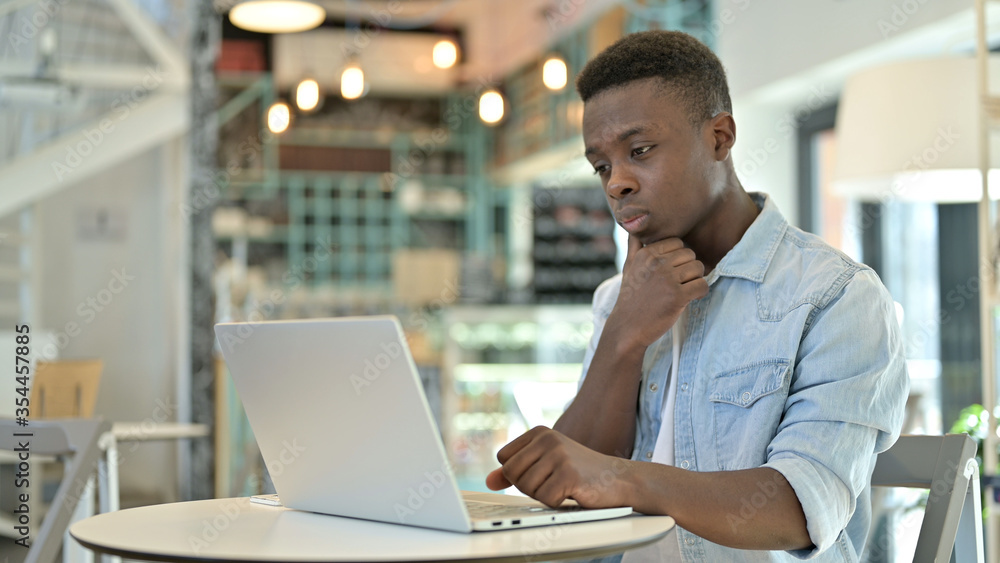 Pensive Young African Man Thinking and working on Laptop in Cafe Pensive Young African Man Thinking and working on Laptop in Cafe