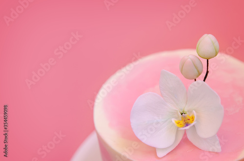 Cake decorated with sugar flower orchid close-up top view. Pink marble cake stands on a round white stand on a pink background. Beautiful dessert decorated with flowers.