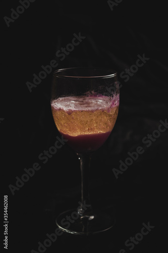 Sparkling wine in a cocktail with red fruit coloring, freshly served in a small glass, the foam and the gas can be perceived perfectly.