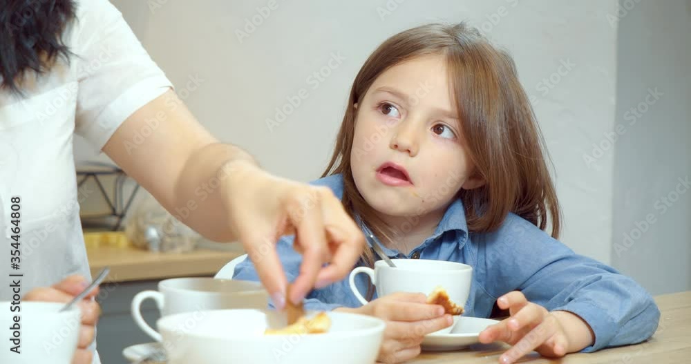 Portrait of a cute little girl eating cookies during breakfast with mom in the kitchen Portrait of a cute little girl eating cookies during breakfast with mom in the kitchen