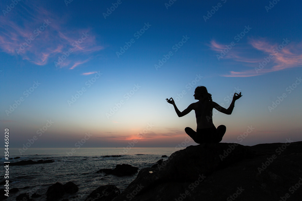 Silhouette of woman yoga in Lotus position on the shore of ocean at amazing evening.