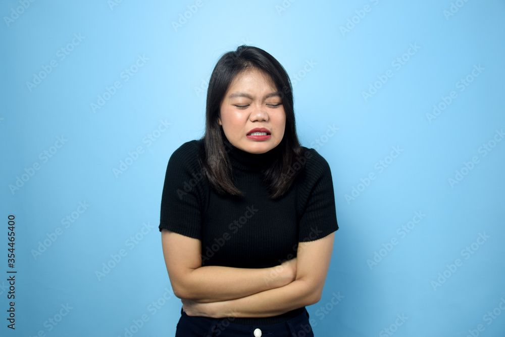 Portrait of Young beautiful asian women wearing black turtle neck shirt with blue isolated background, Stomachache Gesture Portrait of Young beautiful asian women wearing black turtle neck shirt with blue isolated background, Stomachache Gesture