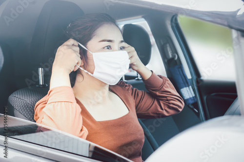 Asian woman sitting in a car wearing protective mask before driving car during covid-19 pandemic, new normal lifestyle concept background
