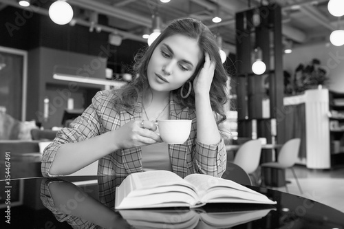 Young beautiful woman drinks coffee and reading book in cafe