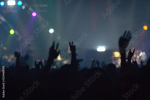 Concert crowd attending a concert, people silhouettes are visible, back lit by stage lights. Raised hands
