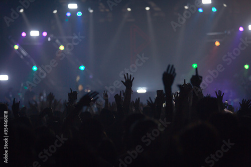 Concert crowd attending a concert, people silhouettes are visible, back lit by stage lights. Raised hands