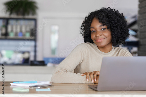 Pretty african girl posing at cafe while working with laptop