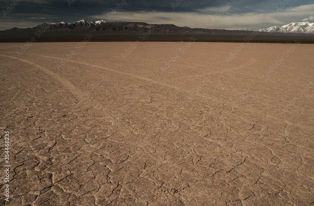 Fototapeta premium Textured ground. Arid desert field landscape with the mountains in the background. Vast clay terrain in dry weather creating texture and pattern.