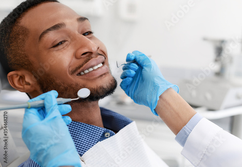 Smiling african man and female dentist hands with tools