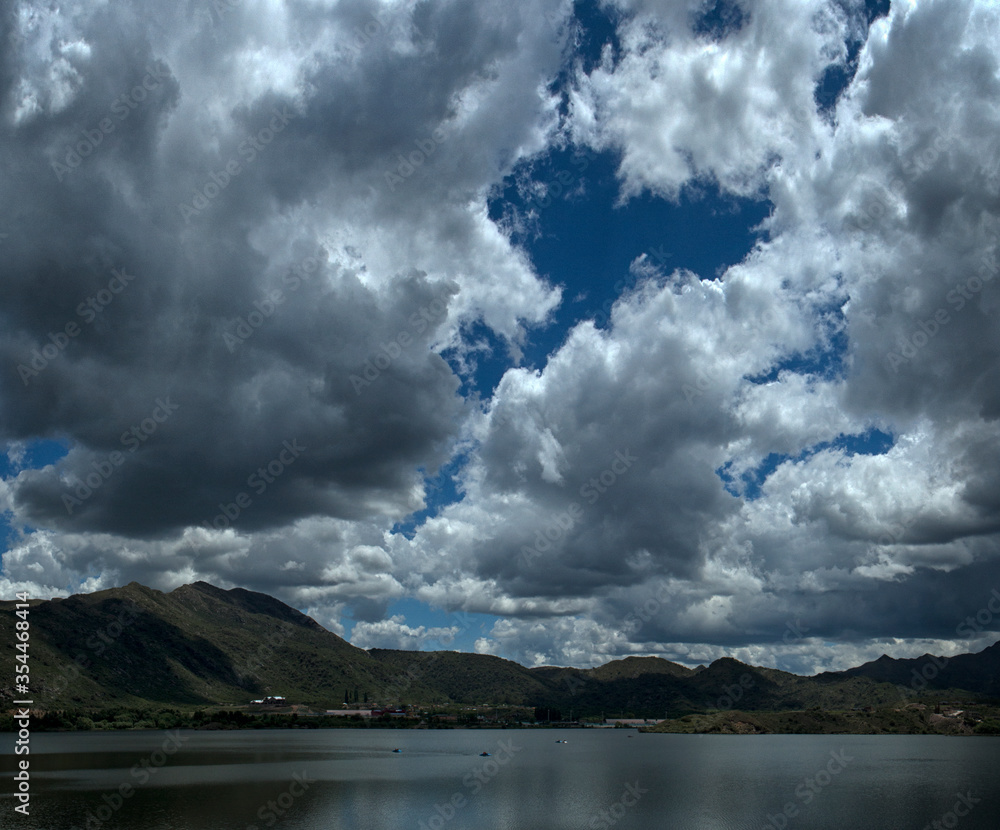 Beautiful lake surrounded by forest and hills under a dramatic sky with foamy clouds and the reflection in water
