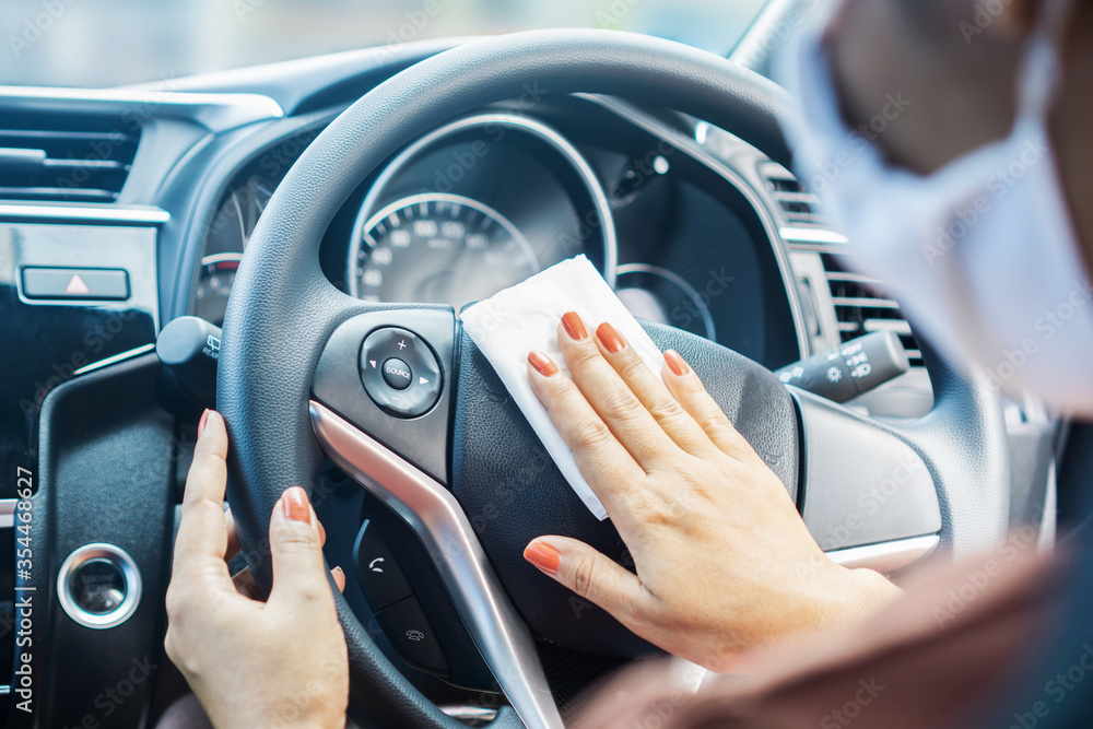 woman hand cleaning on steering wheel during covid-19 or corona virus pandemic, new normal lifestyle concept