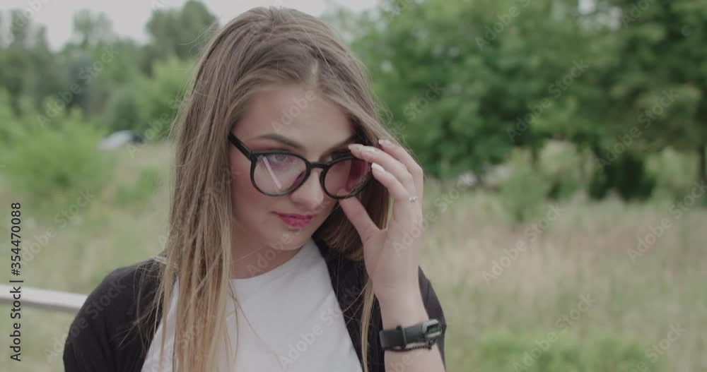 Girl with blowing hair looking at camera with smile on face and corrects glasses Girl with blowing hair looking at camera with smile on face and corrects glasses