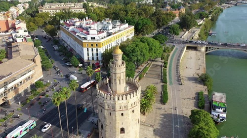Aerial panning shot of tourists at tower by river and street in city, drone flying over famous landmark on sunny day - Seville, Spain