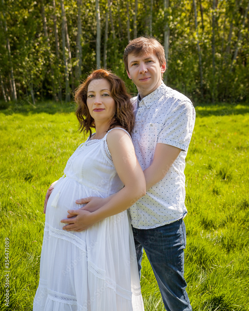 Happy beautiful pregnant woman with his husband in the green park sunny day. Happy beautiful pregnant woman with his husband in the green park sunny day.