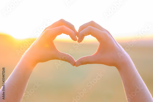 Hands making heart shape with sunset. Close up of woman hands making heart shape gesture. High quality photo .