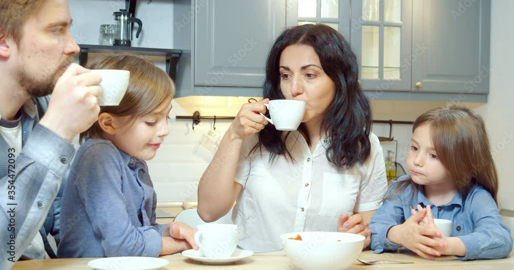 Happy family mom and dad with two cute children drinking tea with homemade cookies while spending time together in the kitchen at home. Happy family mom and dad with two cute children drinking tea with homemade cookies while spending time together in the kitchen at home.