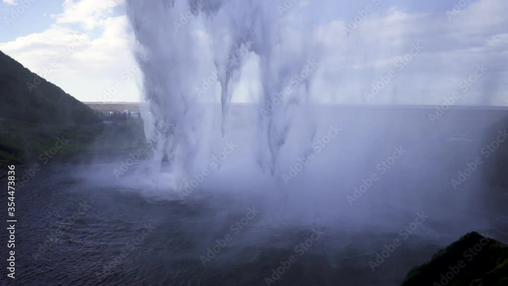 Great view from under Seljalandsfoss waterfall, iceland, on a sunny summer day. View of water tumbling down, cliffs to the left, and view out to the flat horizon. Great view from under Seljalandsfoss waterfall, iceland, on a sunny summer day. View of water tumbling down, cliffs to the left, and view out to the flat horizon.