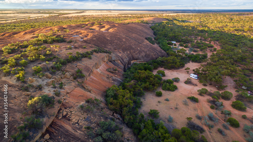 Oblique drone view of a 4WD and a caravan in at a free camp near a granite outcrop in the Australian outback.
