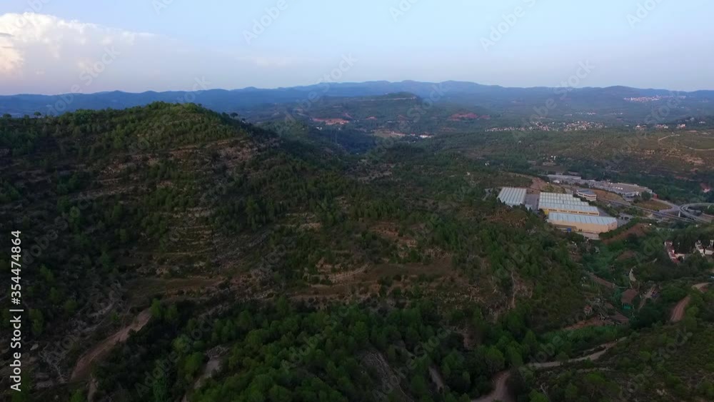 Aerial panning shot of green landscape with buildings against sky, drone flying over forest - Montserrat, Spain Aerial panning shot of green landscape with buildings against sky, drone flying over forest - Montserrat, Spain