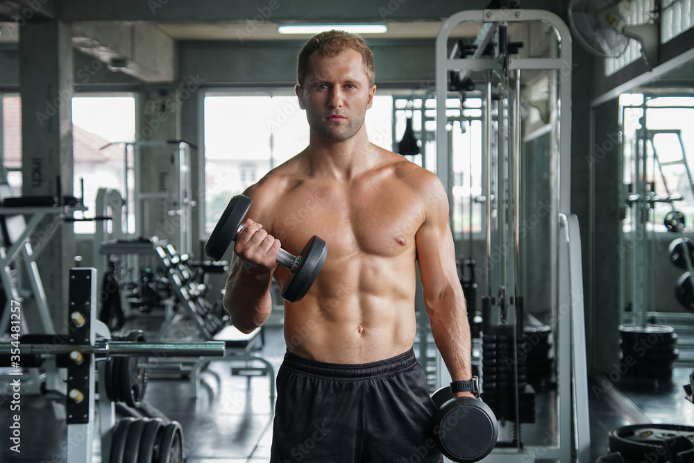 Young handsome muscular man working out with dumbbells. Strong bodybuilder in the gym fitness Young handsome muscular man working out with dumbbells. Strong bodybuilder in the gym fitness