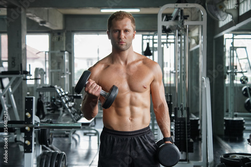 Young handsome muscular man working out with dumbbells. Strong bodybuilder in the gym fitness