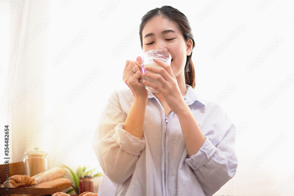 Young Asian woman in the kitchen drinking milk for breakfast, Healthy food concept Young Asian woman in the kitchen drinking milk for breakfast, Healthy food concept