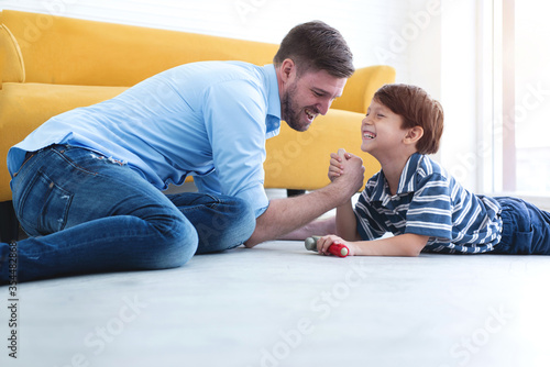 Happy father and son playing arm wrestle with his father and smile, lying on the floor, spending time together at home