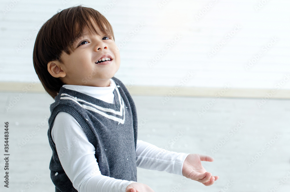 Cute boy having fun playing with fake snowflakes in room, looking up to something Cute boy having fun playing with fake snowflakes in room, looking up to something