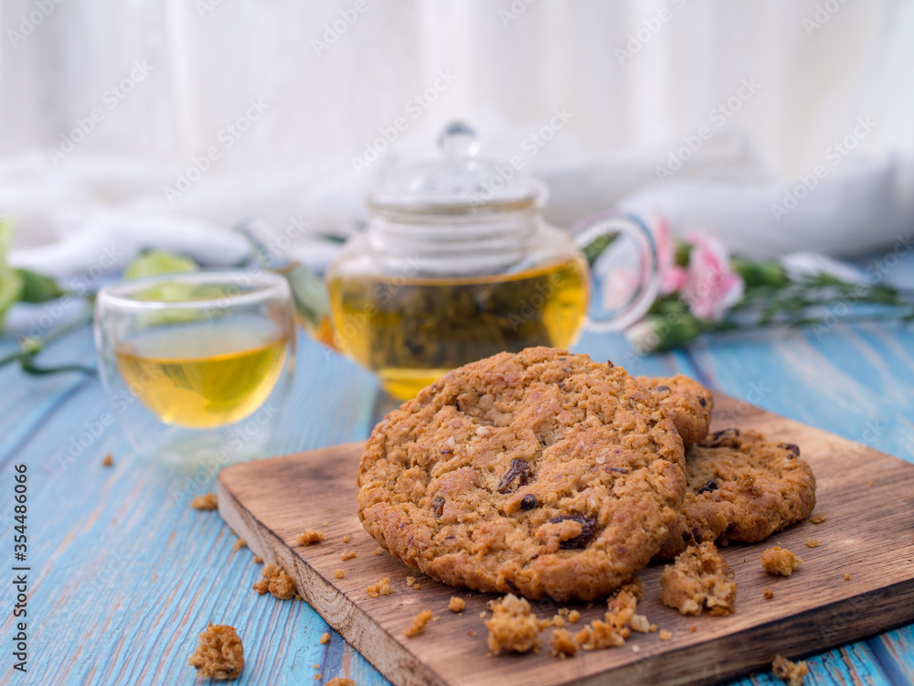 Fototapeta premium Tasty chocolate chip cookies stacked on a board served with tea and teapot on blue wooden table.Organic homemade snacks for healthy breakfast.Space for text and copy space