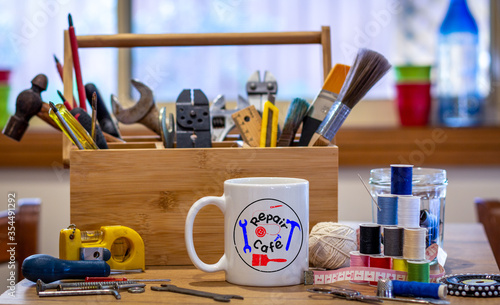 Schilderij op canvas Repair Cafe logo on a cup surrounded by repair tools on table in cafe used as a