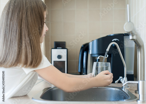 Child pouring fresh reverse osmosis purified water in kitchen at home. Drinking tap water. Consumption of tap water contributes to the saving of water in plastic bottles. Protection of the environment