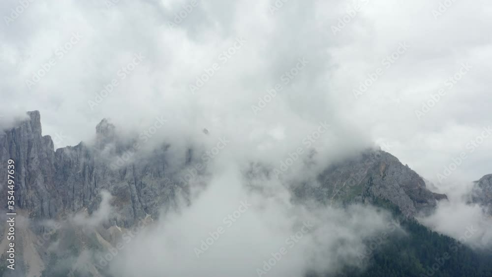 Aerial shot of rocky mountain range amidst clouds, drone flying backward over landscape against sky - Dolomites, Italy Aerial shot of rocky mountain range amidst clouds, drone flying backward over landscape against sky - Dolomites, Italy