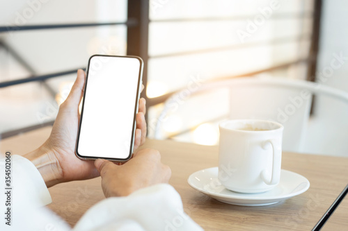 cell phone mockup image blank white screen.woman hand holding texting using mobile on desk at coffee shop.background empty space for advertise.work people contact marketing business,technology