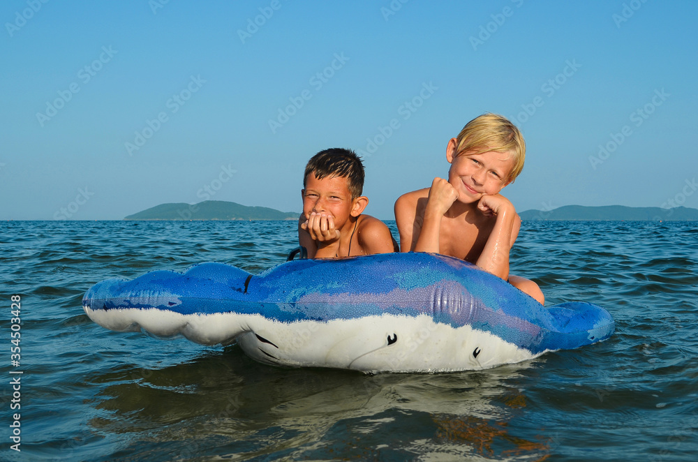 Happy two caucasian children swim in the sea on inflatable circles on summer holidays lifestyle. Active leisure for health and sports outdoor.