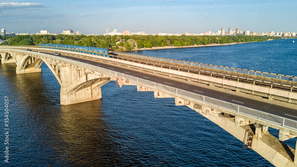 Aerial drone view of Metro railway bridge with train and Dnieper river from above, skyline of city of Kyiv, Kiev cityscape, Ukraine
