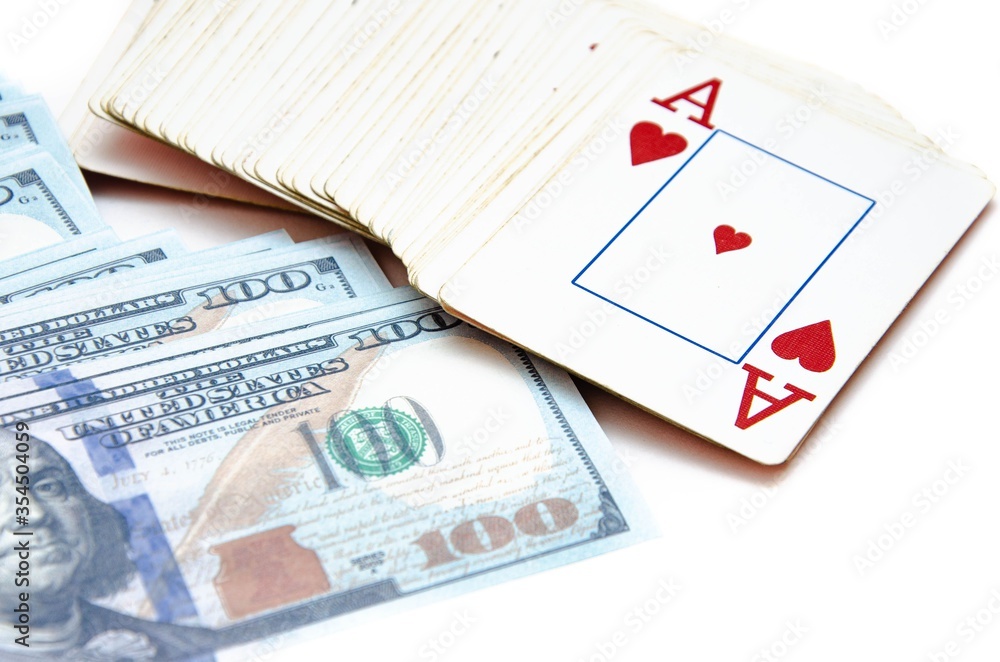 Dollars and playing cards. Banknotes with a face value of 100 dollars are lying on a white background in a pile, a bunch of flowers, on top is a deck of cards, an ace of hearts from above Dollars and playing cards. Banknotes with a face value of 100 dollars are lying on a white background in a pile, a bunch of flowers, on top is a deck of cards, an ace of hearts from above