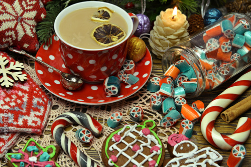 Jar with candy, cup of tea and gingerbread cookie on festive table.