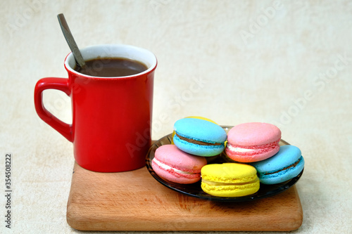 Colorful french Sweet Pastries Macaroons on glass table and red coffee mug on wooden tray.