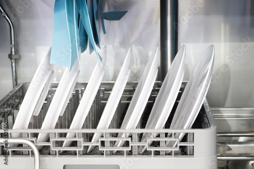 The automatic dishwasher with white clean dishes in basket .For restaurant.