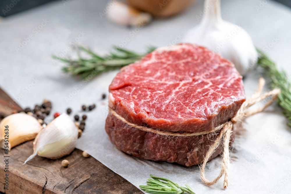Raw beef filet Mignon steak on a wooden Board on paper with ingredients for grilling, close up Raw beef filet Mignon steak on a wooden Board on paper with ingredients for grilling, close up