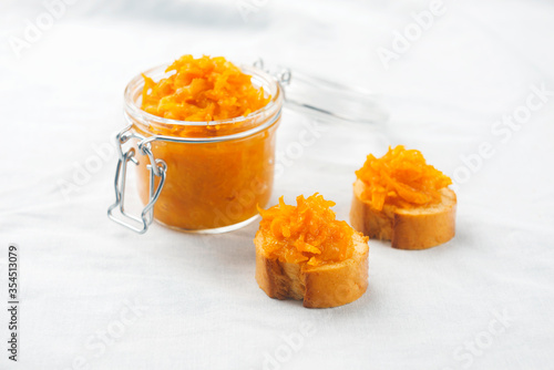 A jar of orange confiture with two pieces of French baguette on white tablecloth,