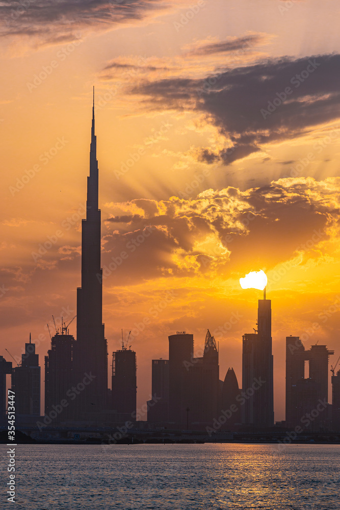 Obraz premium Dubai skyline at sunset during golden hour, sun setting over Dubai skyline; silhouette of Dubai skyline