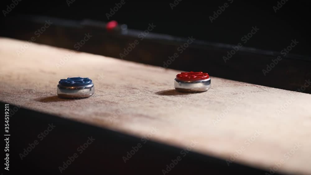 Shuffleboard disc sliding on sandy board between two pucks in slow motion during game Shuffleboard disc sliding on sandy board between two pucks in slow motion during game