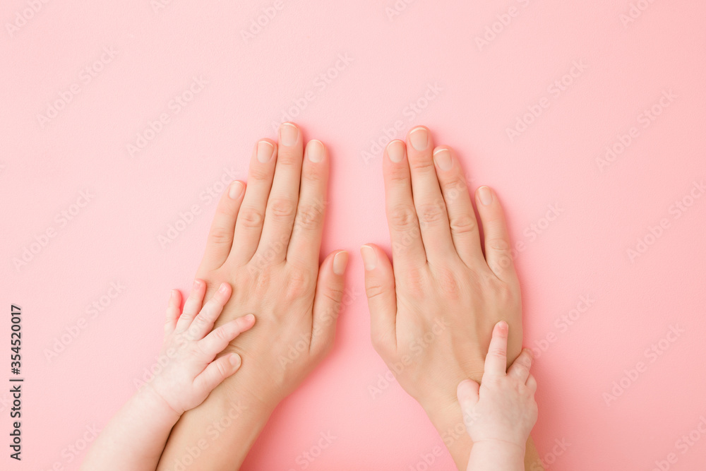 Baby hands touching young mother hands on light pink table background. Pastel color. Closeup. Family concept. Top down view. Baby hands touching young mother hands on light pink table background. Pastel color. Closeup. Family concept. Top down view.