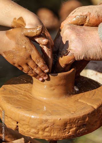Hands of a boy and a man sculpt clay dishes.