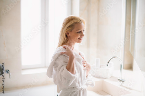 Beautiful woman enjoying in hotel. Young happy women in bathrobe use the cream for the body.	