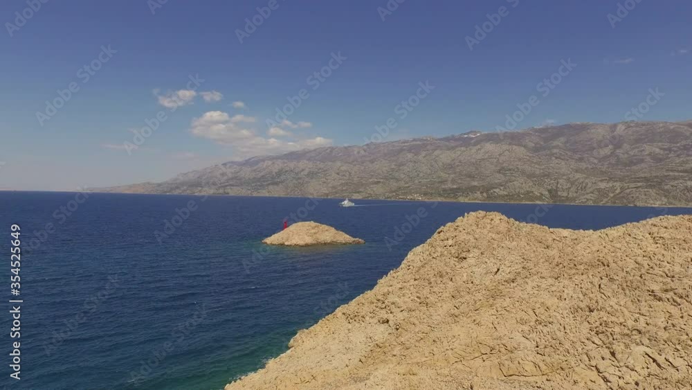 Aerial shot of coastline with lighthouse on rocky island, drone flying forward towards ship near mountains on sunny day against sky - Pag, Croatia Aerial shot of coastline with lighthouse on rocky island, drone flying forward towards ship near mountains on sunny day against sky - Pag, Croatia