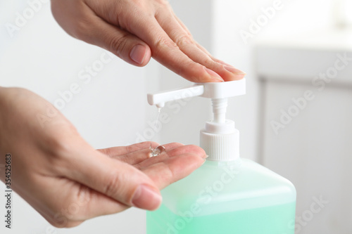 Woman applying antiseptic gel on hand indoors, closeup