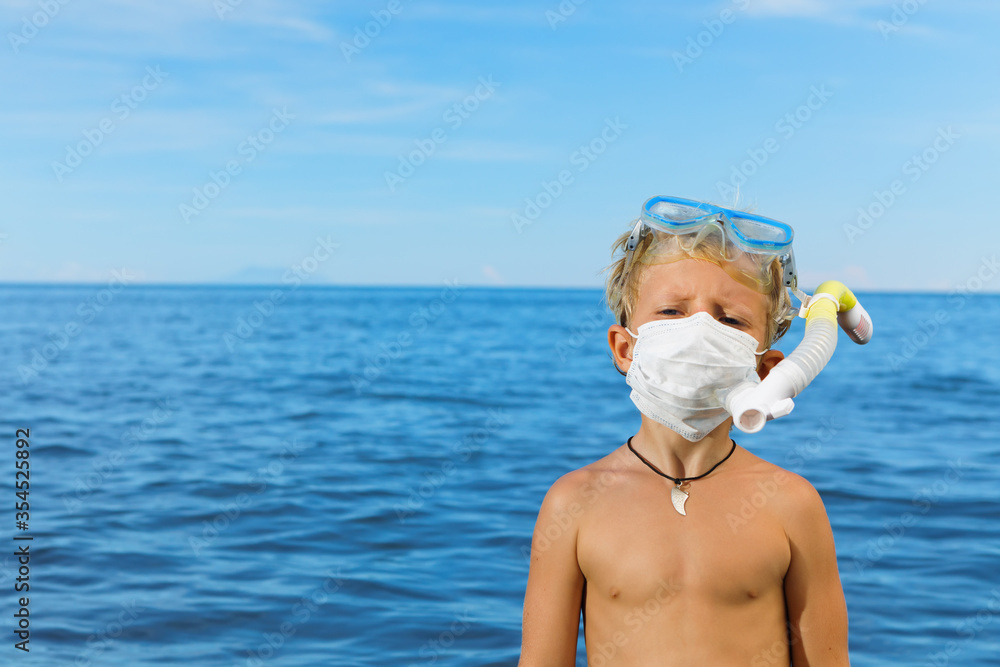 Boy in snorkeling mask wear surgical face mask on sea beach. Cancelled cruises, tours due coronavirus COVID 19 world epidemic. Travel ban for family vacation, tourism industry crisis at summer 2020